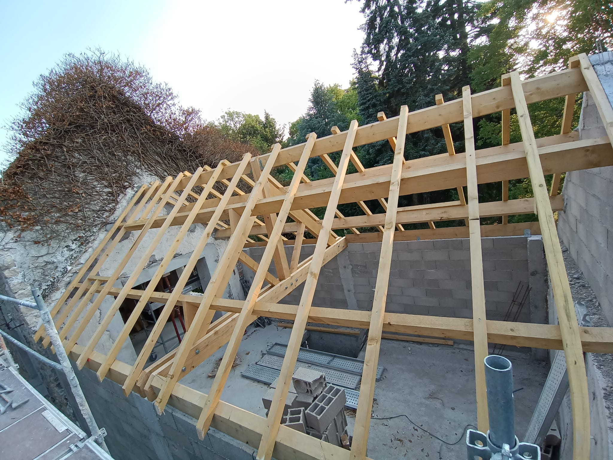 Extension de maison en cours : charpente bois neuve entre un mur en blocs béton et un mur ancien