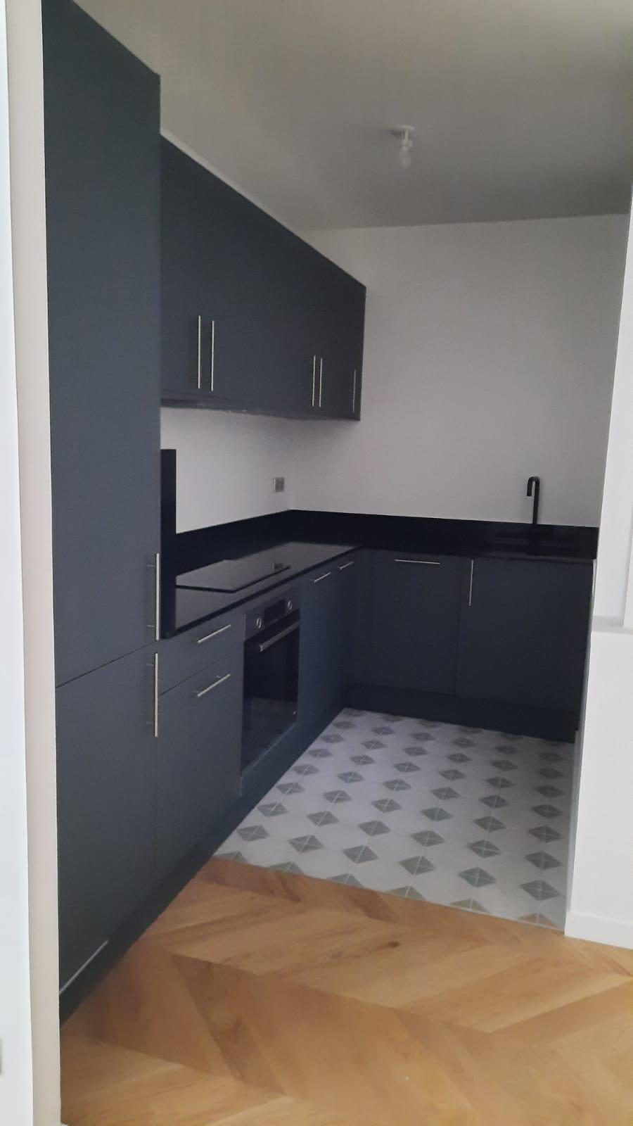 Cuisine anthracite livrée : plan de travail noir, carreaux de ciment au sol et parquet à chevrons dans la pièce voisine. Chantier réel des équipes partenaires.