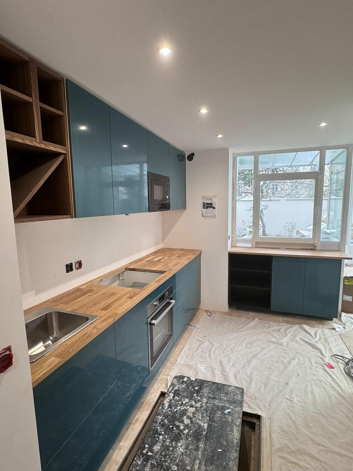 Cuisine bleu canard en cours de pose, caissons ouverts sans façade à côté des éléments finis. Chantier réel des équipes partenaires.