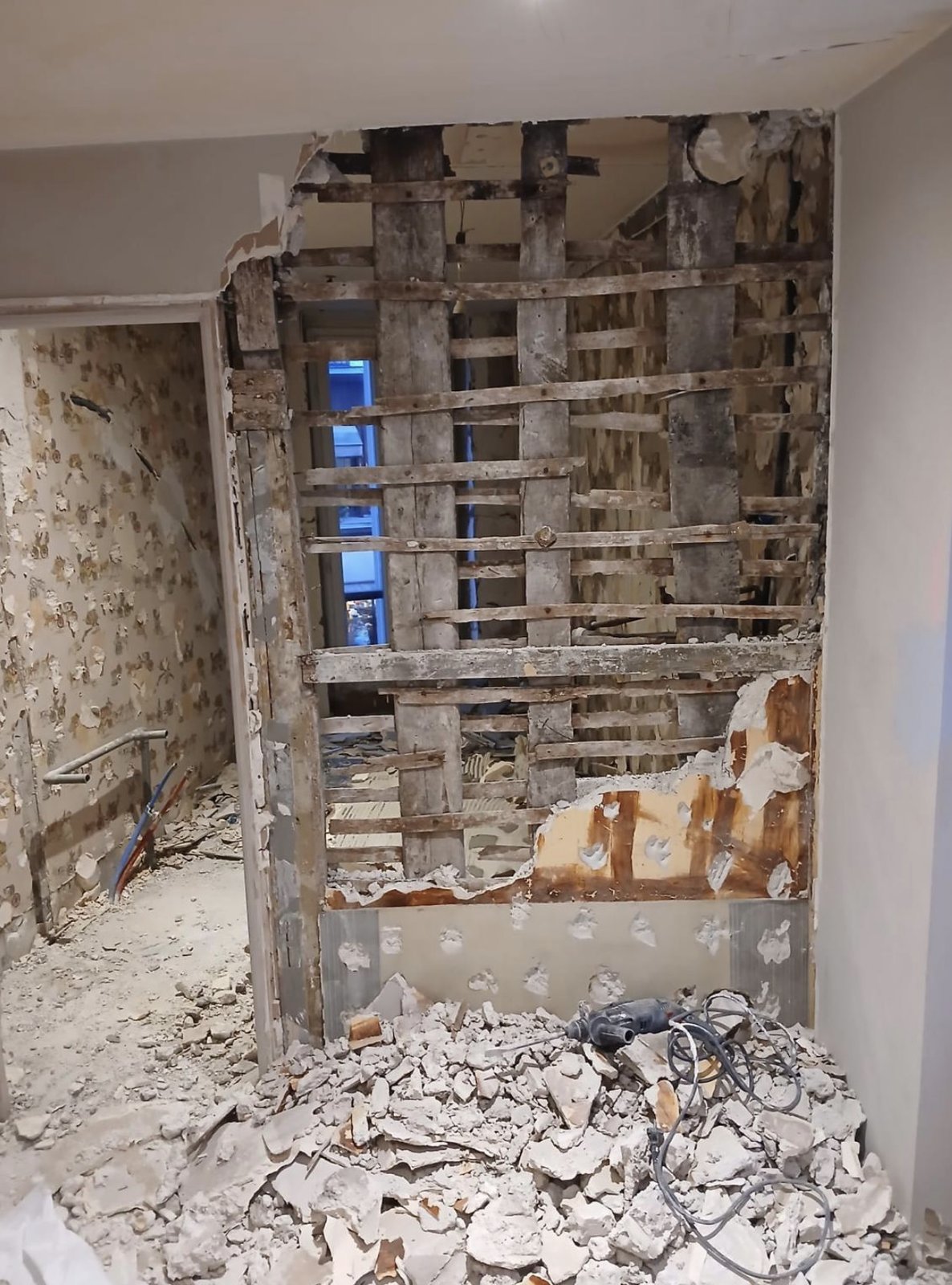 Démolition contrôlée d'un mur en pan de bois : montants et lattis mis à nu, gravats et perforateur au sol, avant la pose du portique