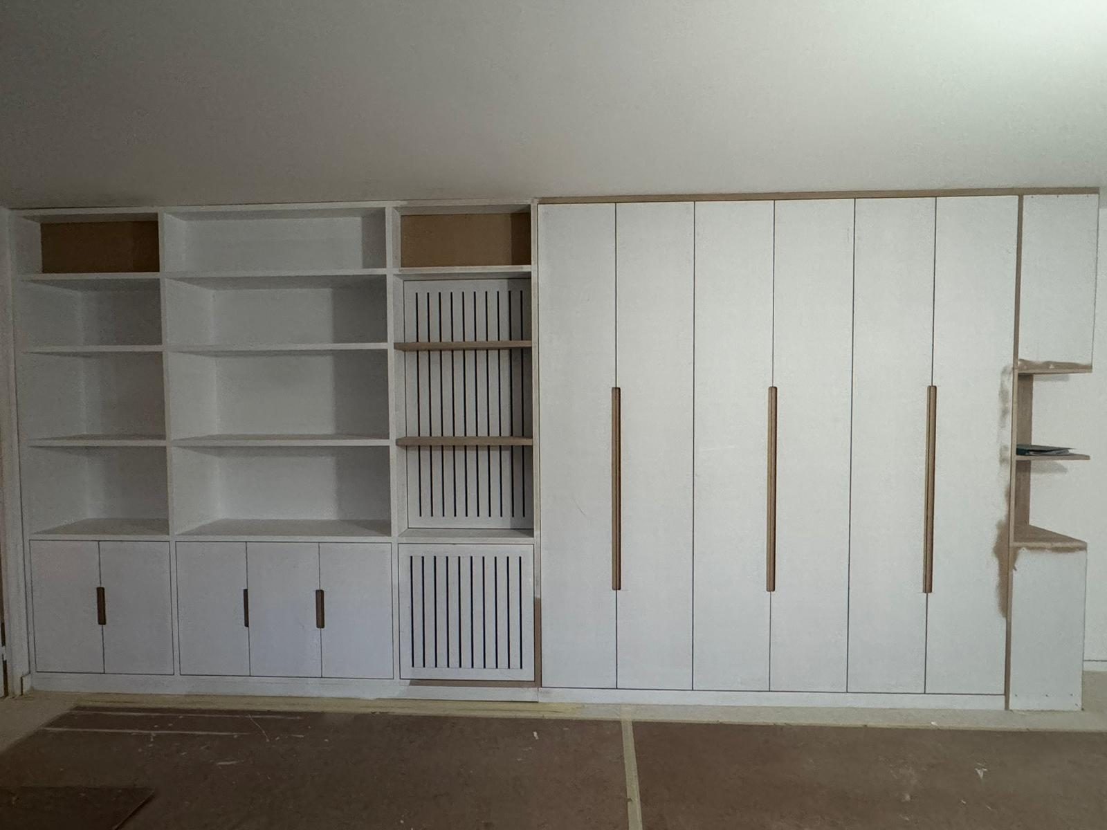 Mur de rangements sur mesure avec étagères ouvertes, portes pleines et habillage à claire-voie devant le radiateur