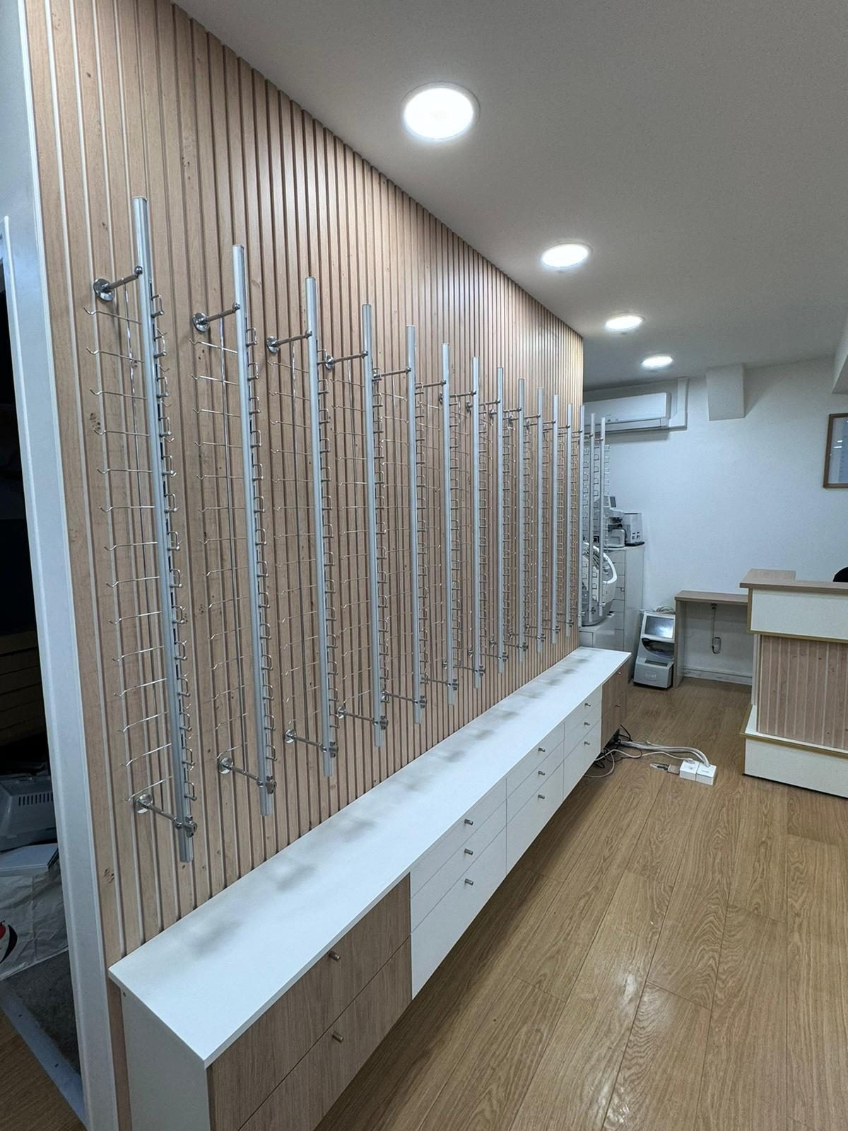Présentoirs muraux sur mesure pour montures : réglettes aluminium fixées sur un mur de tasseaux, meubles à tiroirs en pied. Chantier réel des équipes partenaires.