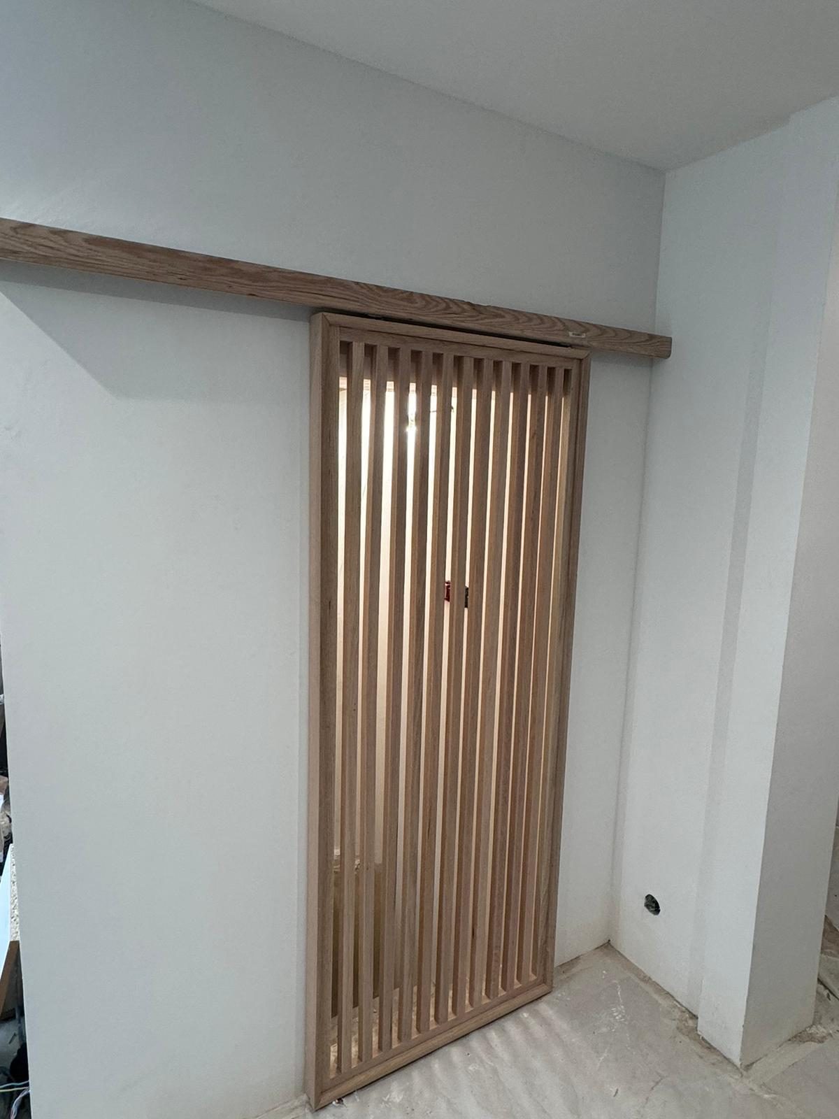 Porte coulissante à claustra de lames verticales en bois clair, rail masqué par un bandeau