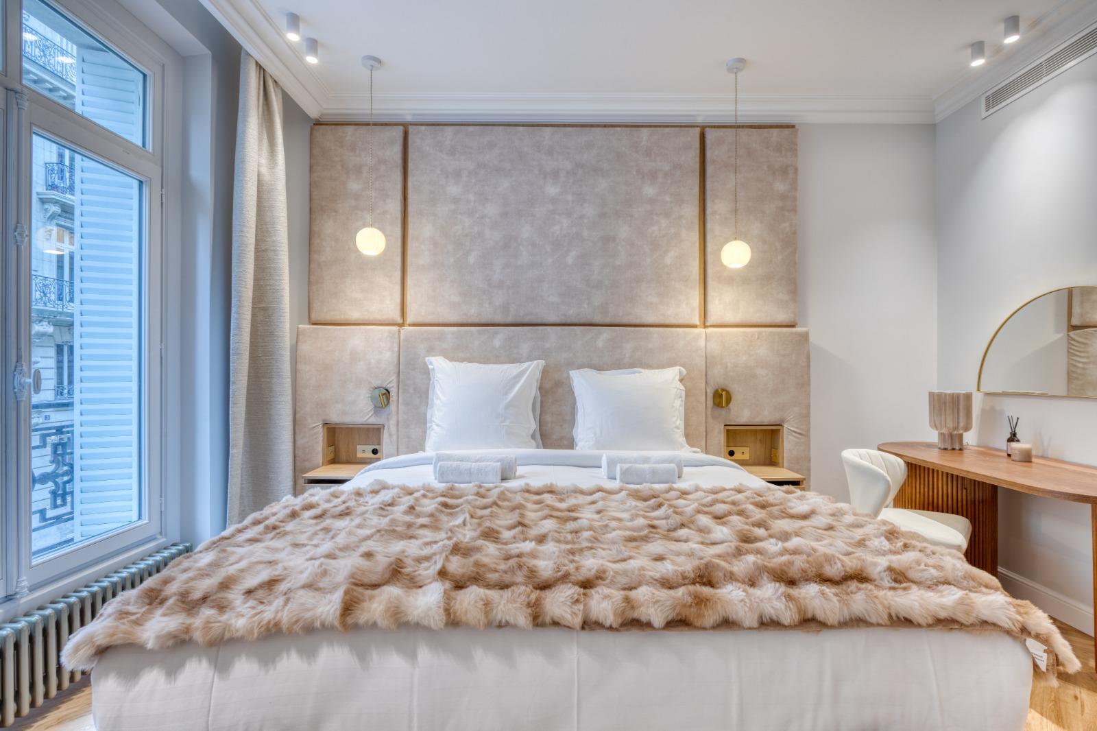 Chambre d'un appartement haussmannien rénové : tête de lit capitonnée, suspensions, bureau en bois sous un miroir