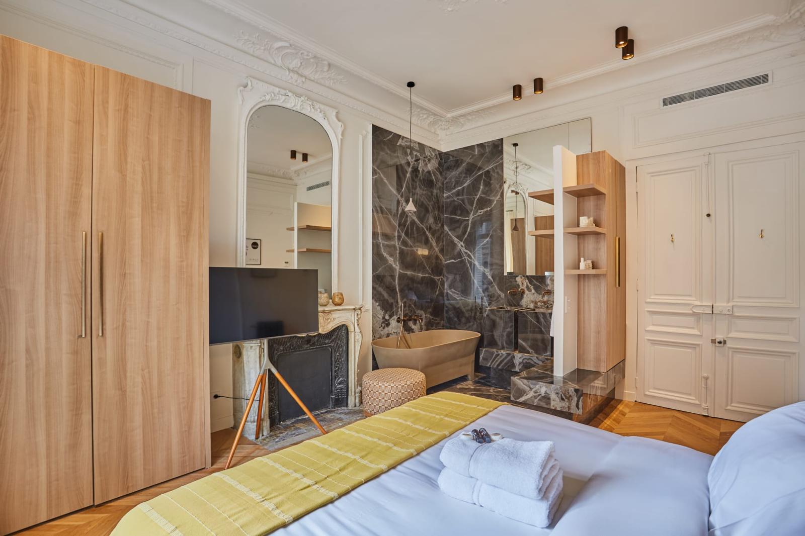 Chambre d'un appartement haussmannien rénové ouverte sur une salle de bain en marbre sombre, cheminée d'origine conservée : un chantier de rénovation piloté jusqu'aux finitions