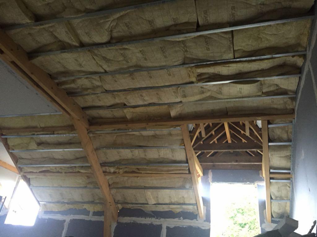 Rénovation énergétique d'un comble : panneaux de laine minérale posés entre les chevrons d'une charpente ancienne, sous la toiture