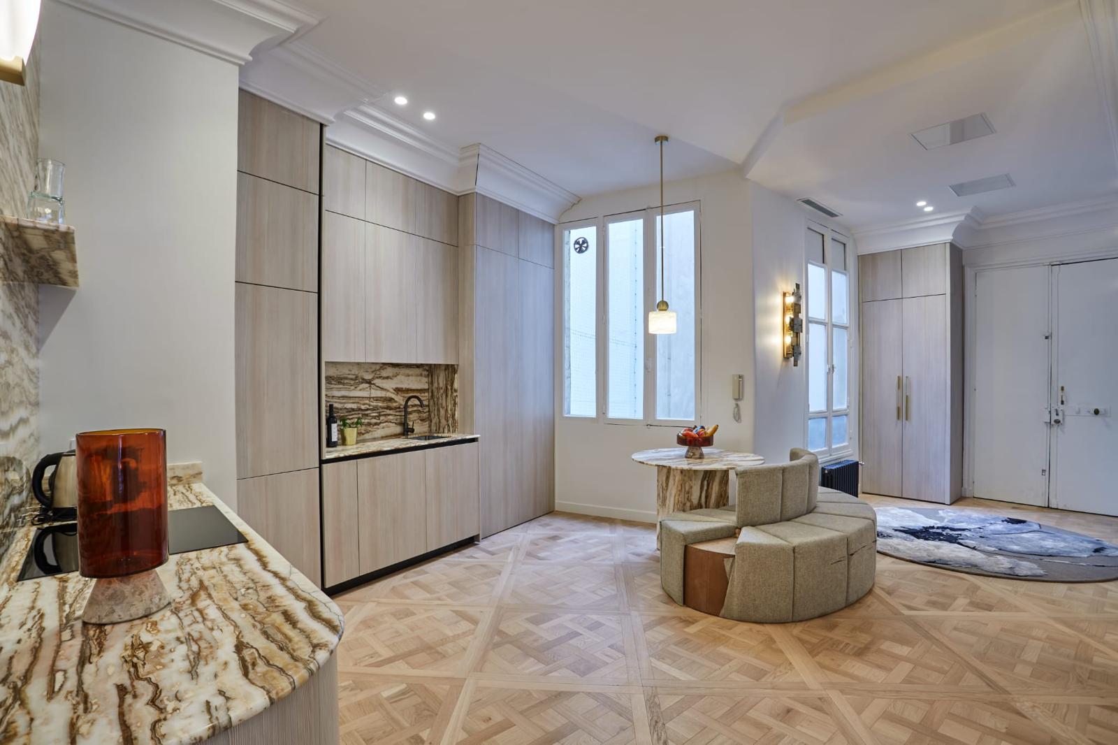 Cuisine ouverte rénovée : colonnes en bois clair, plan de travail en pierre, parquet de Versailles